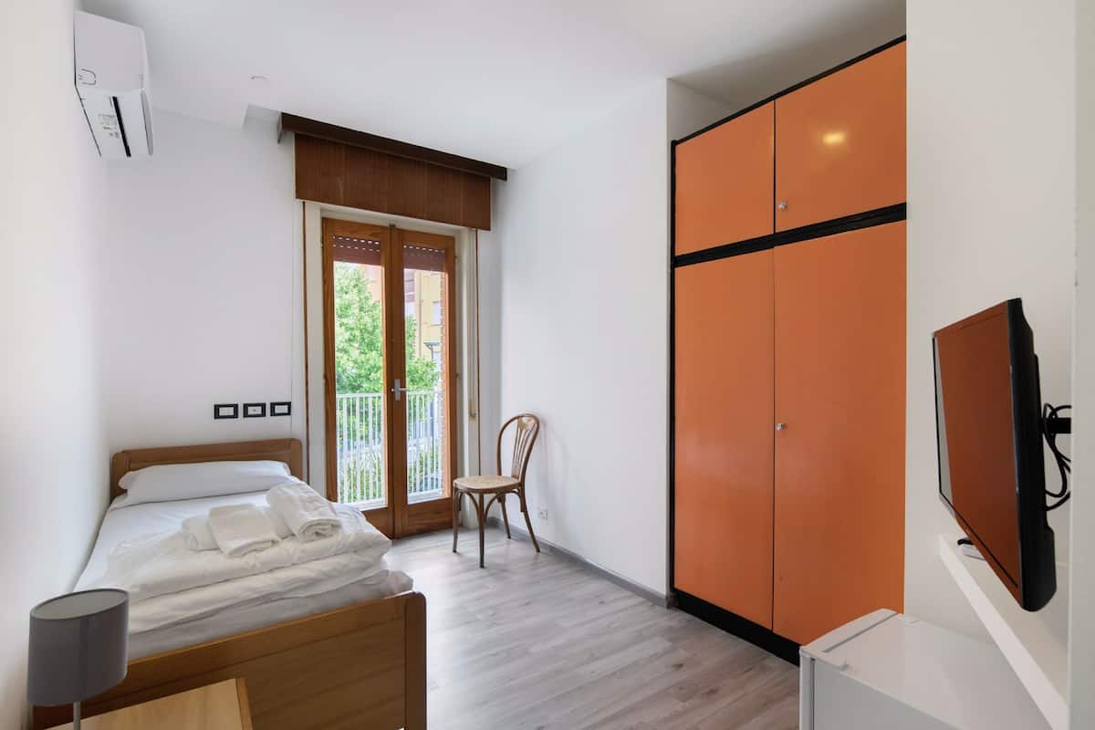 A bedroom with a bed, a chair, an orange wardrobe, and a TV.