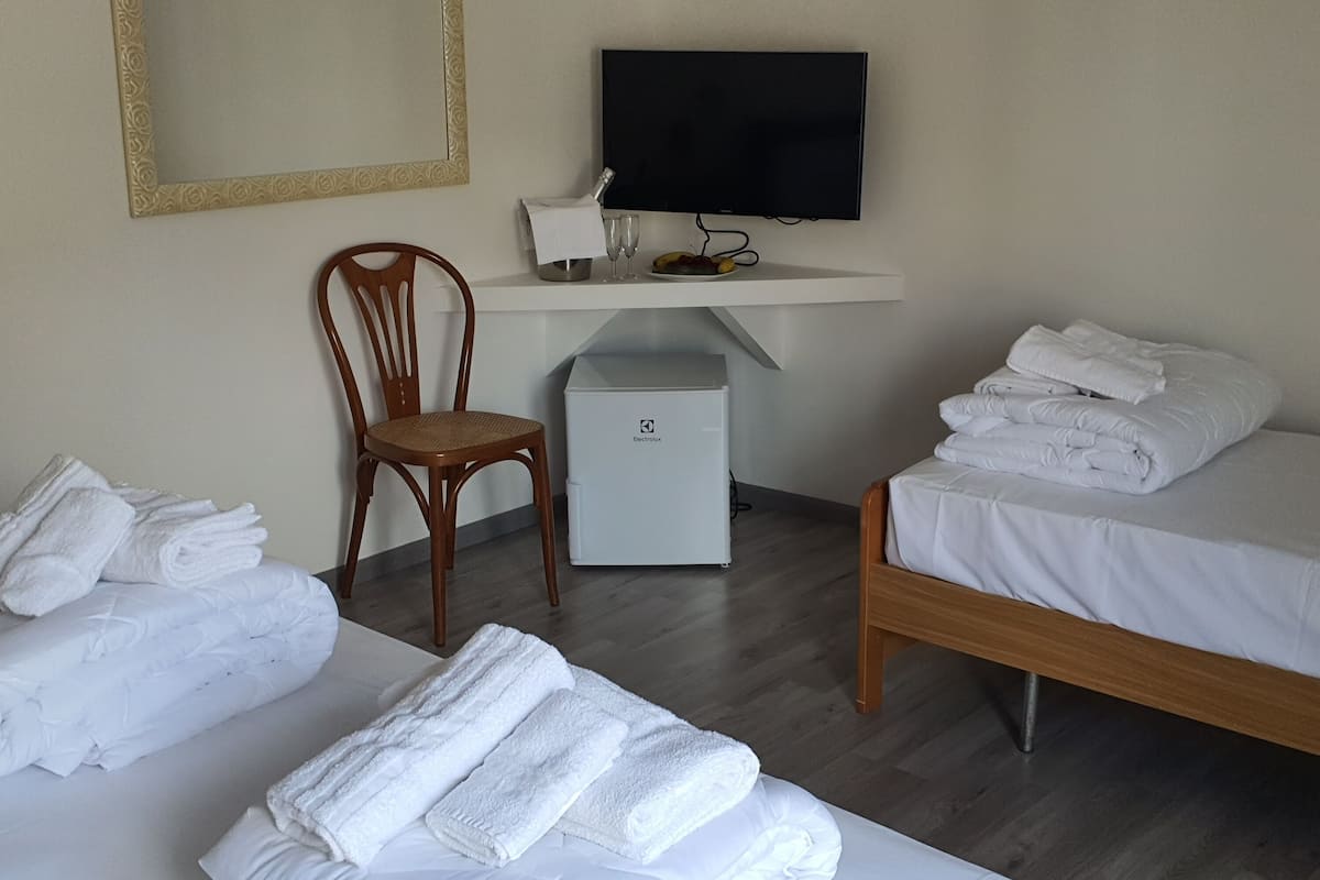 A hotel room with two beds, a desk with a television, a chair, and a minibar.