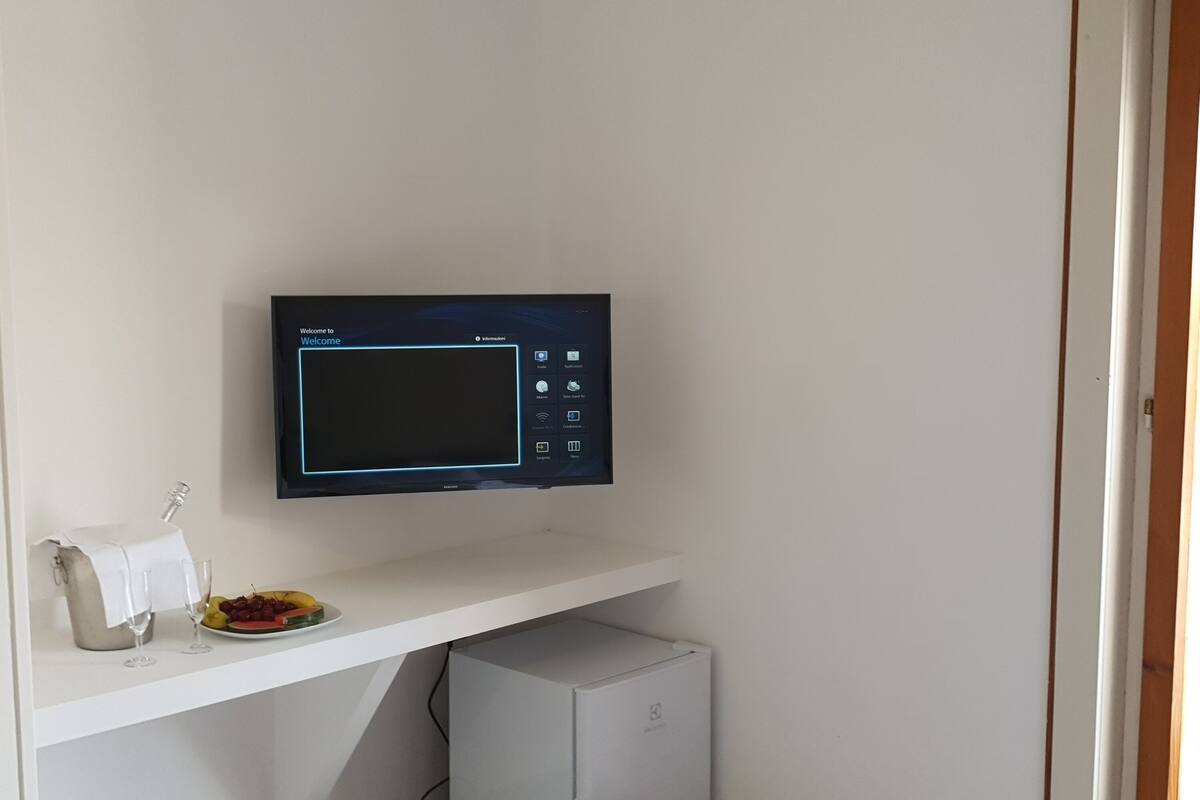 A room with a flat-screen TV mounted on a white wall, a small white cabinet below, and a white door to the right.