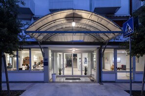 A hotel entrance with a covered walkway, glass doors, and a visible interior with tables and chairs. - Miga Hotel Grado Centro (Grado)