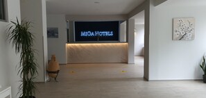 A reception area with a neon sign for MIGA HOTELS, a potted plant, and a vase on the floor. - Miga Hotel Grado Centro (Grado)