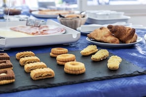 A breakfast buffet with various pastries and bread on a blue tablecloth. - Miga Hotel Grado Centro (Grado)
