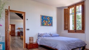 Ein Schlafzimmer mit Holzboden, einem Bett mit blauer Bettdecke, einem Bild an der Wand und einem Fenster mit Holzläden.