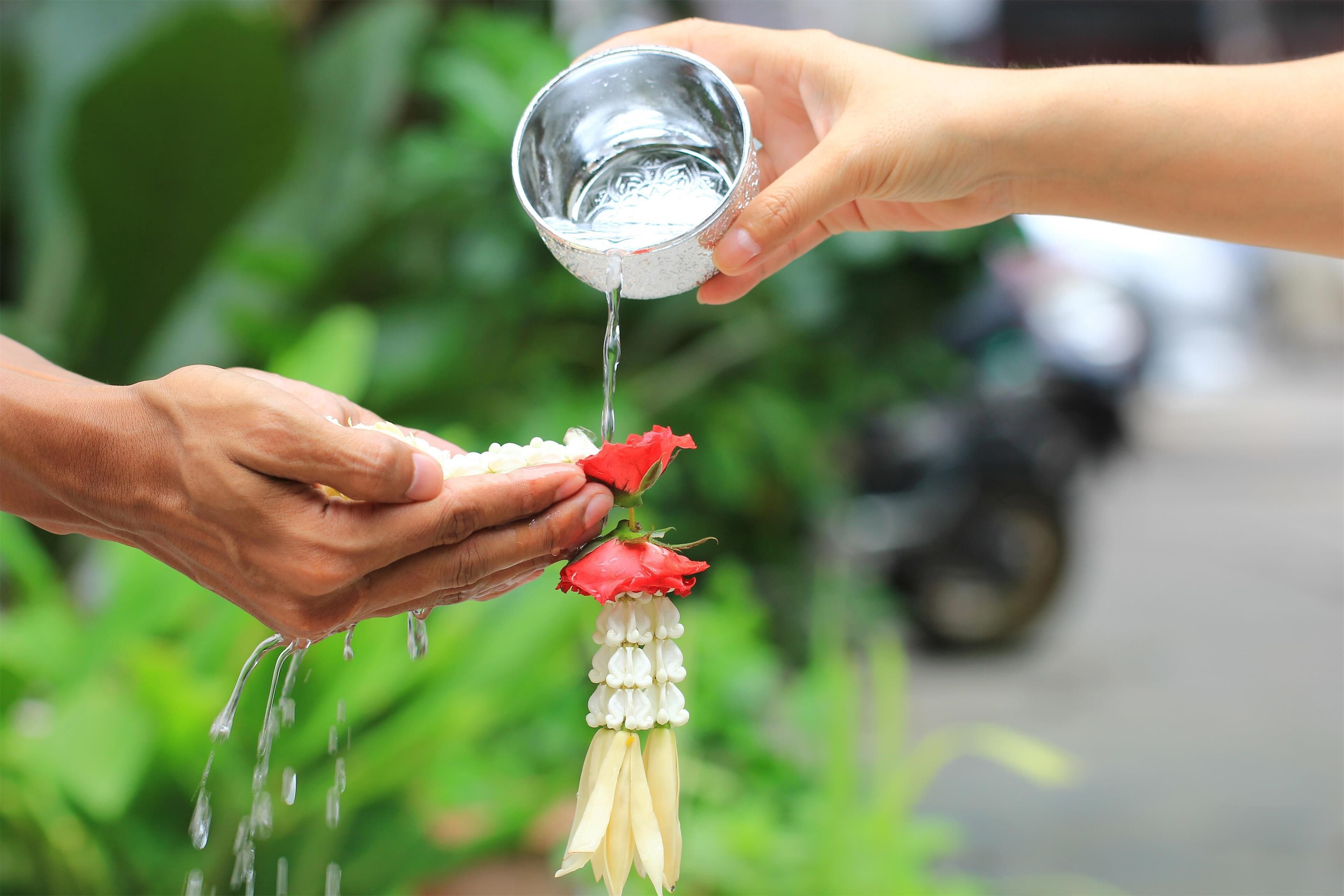 A person holding a flower arrangement with water being poured over it.