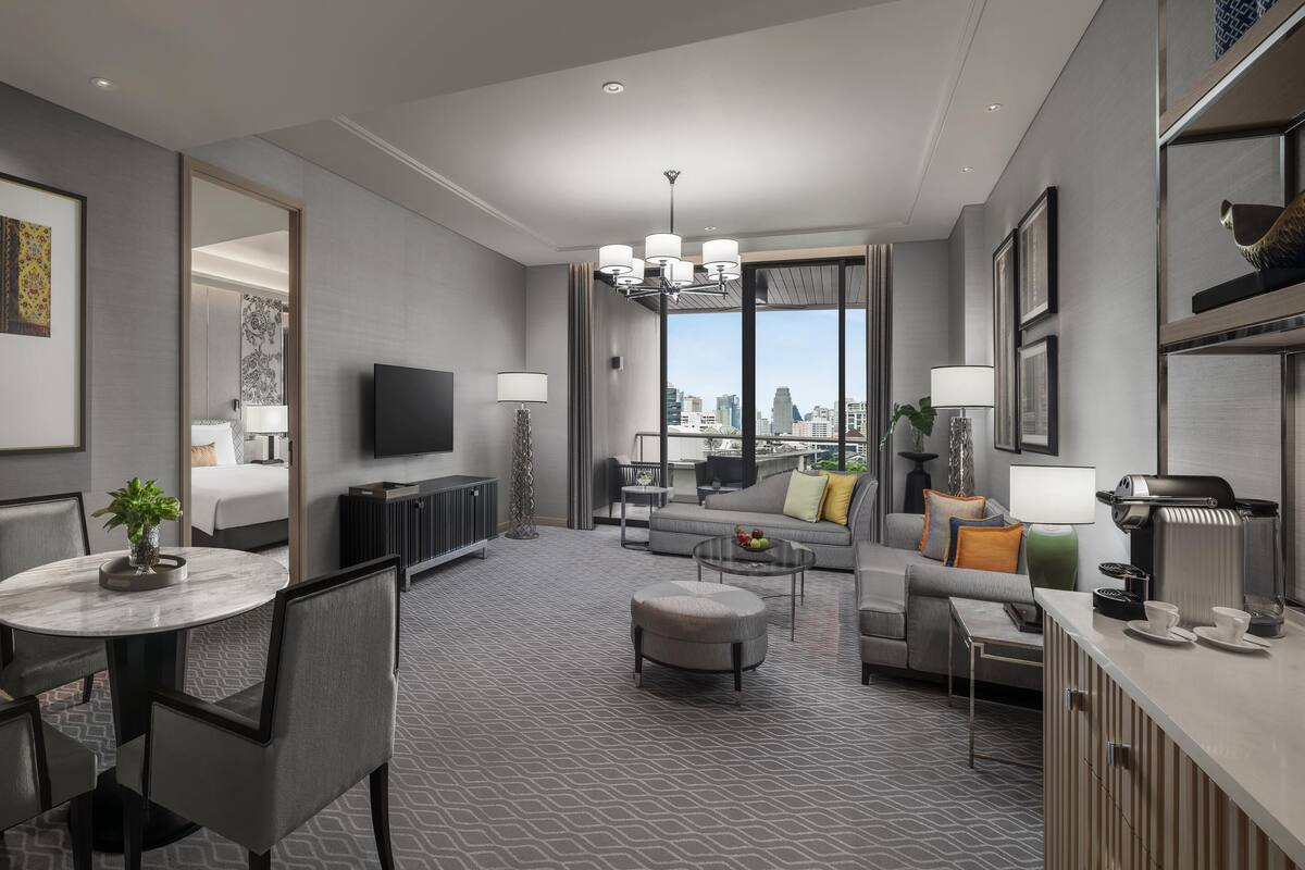 Una habitación de hotel moderna con comedor, sala de estar con sofá y vistas a la ciudad, y kitchenette.