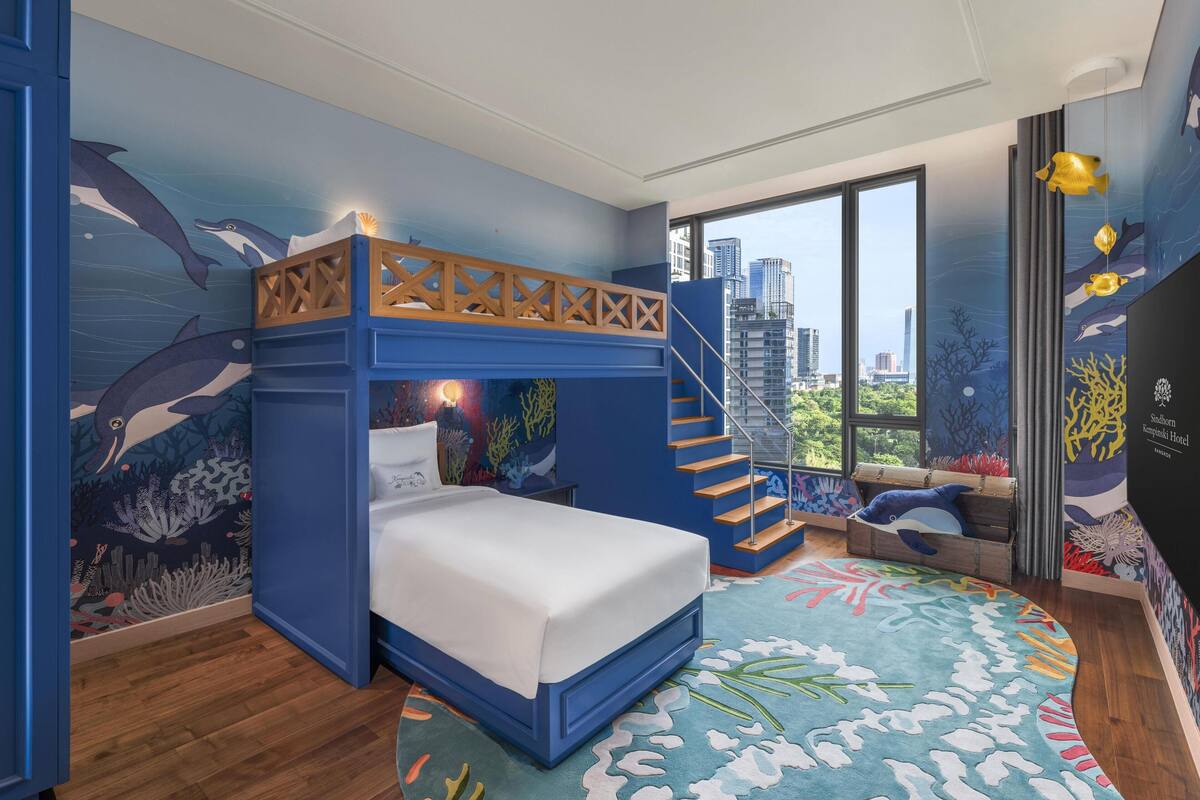 Una habitación con literas, vistas a la ciudad y un mural con motivos marinos.