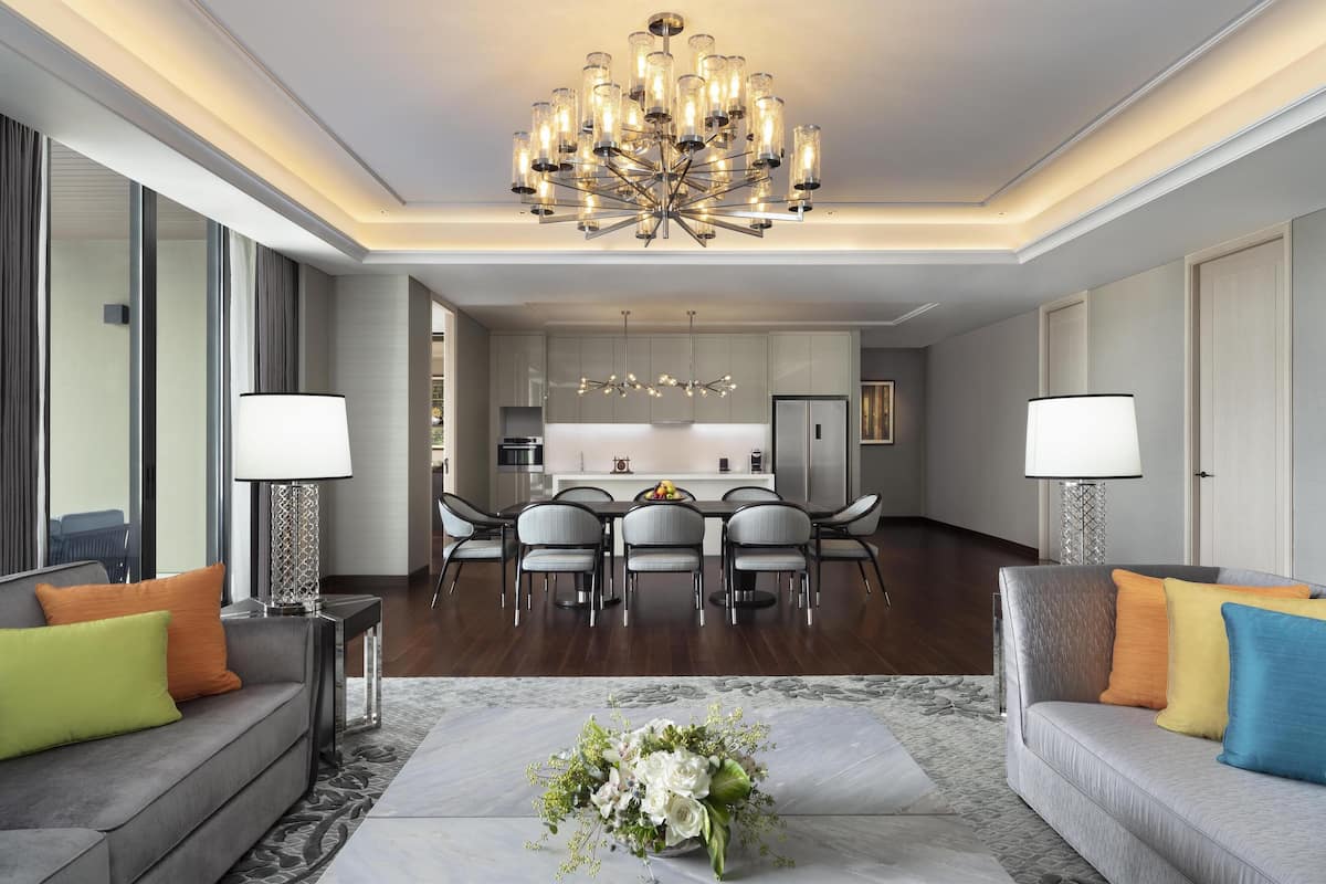 Una sala de estar moderna con comedor, que incluye una araña, sofás grises y una mesa central con sillas.