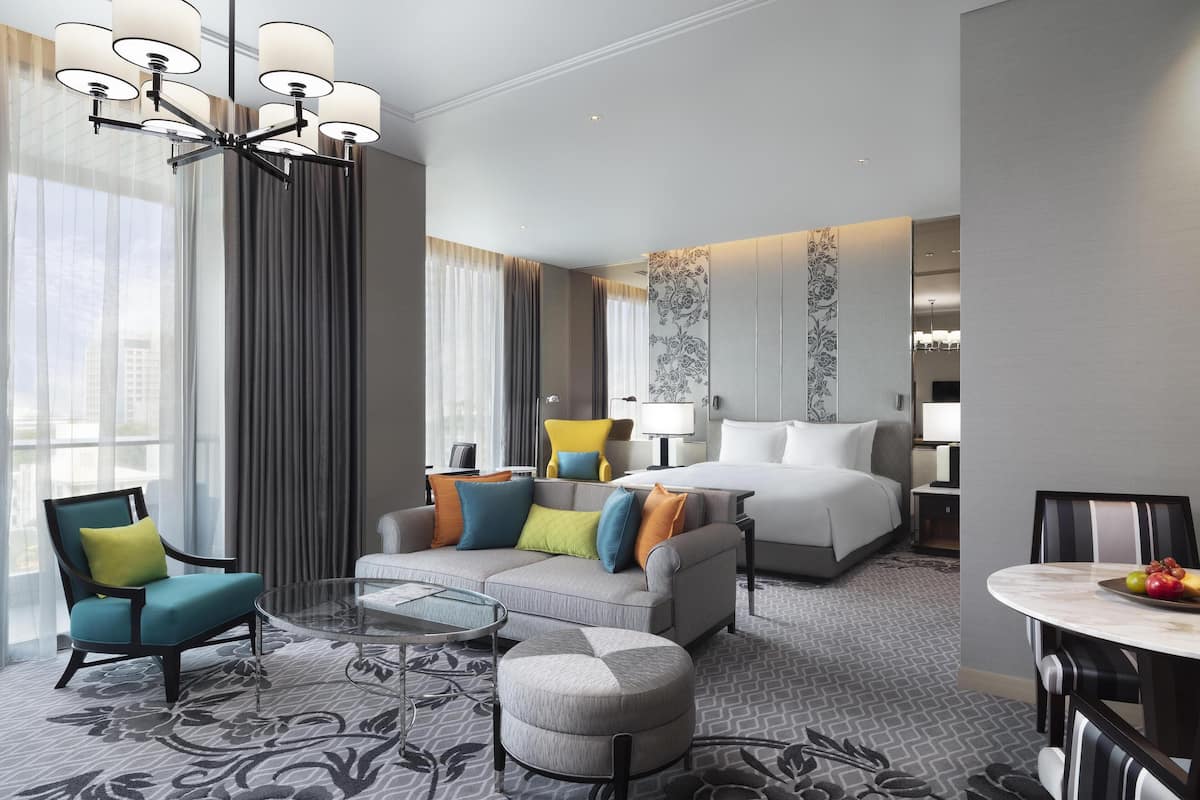Una habitación de hotel moderna con una cama grande, un sofá, una mesa de centro y una mesa de comedor.