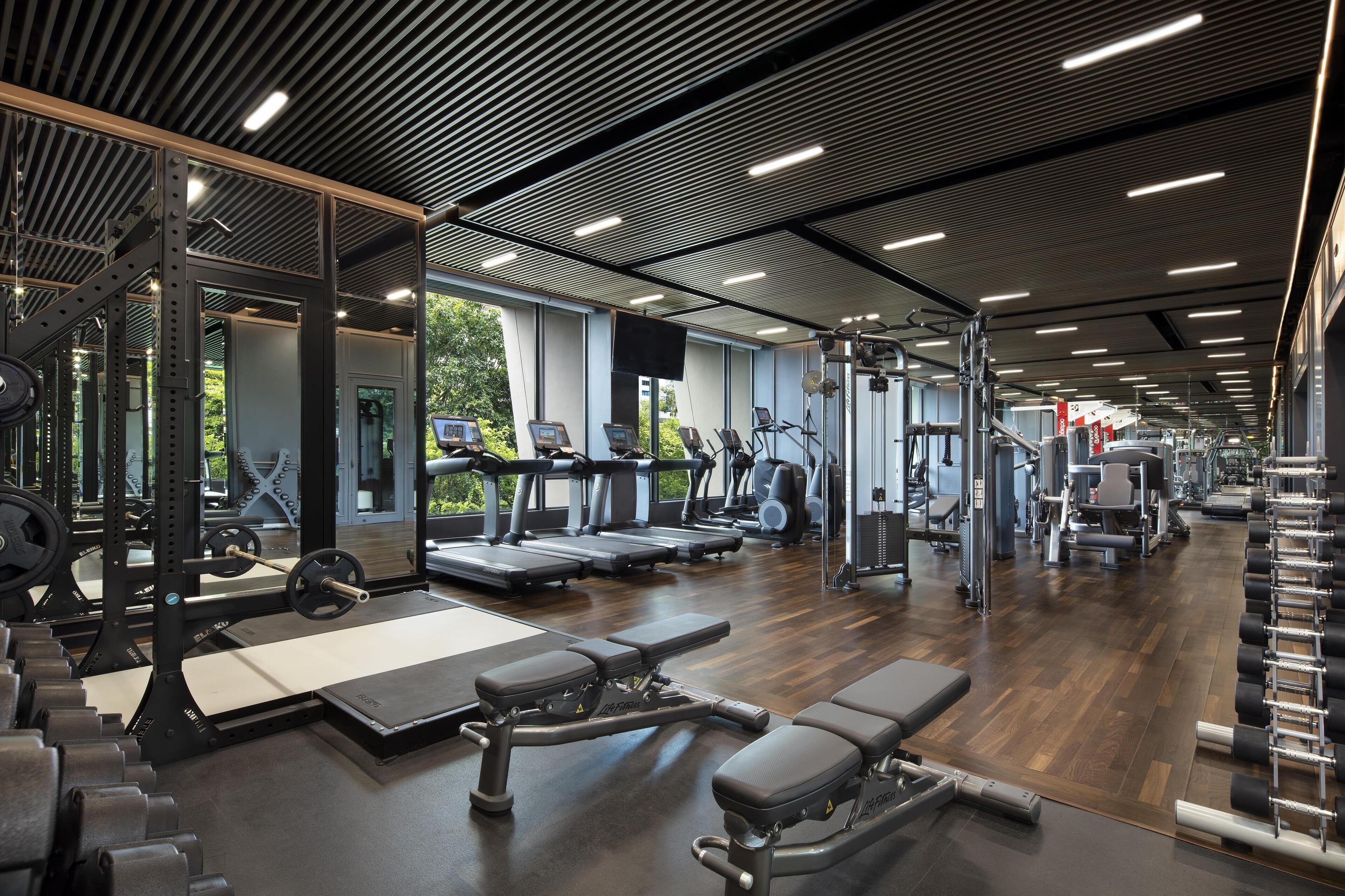 Een moderne sportschool met diverse trainingsapparaten, grote ramen en een houten vloer.