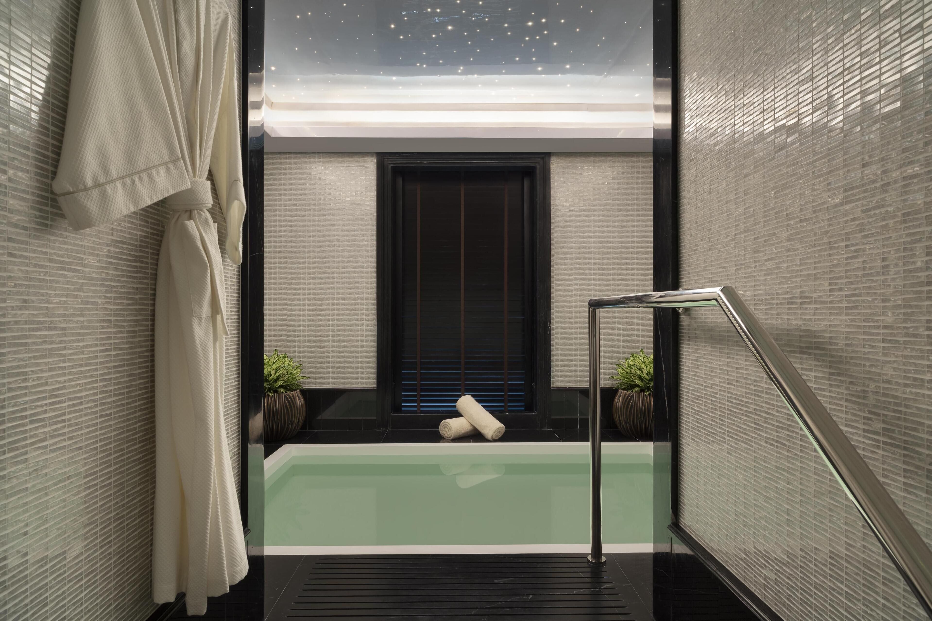 A modern bathroom with a glass-enclosed bathtub, a towel rack, and two potted plants.