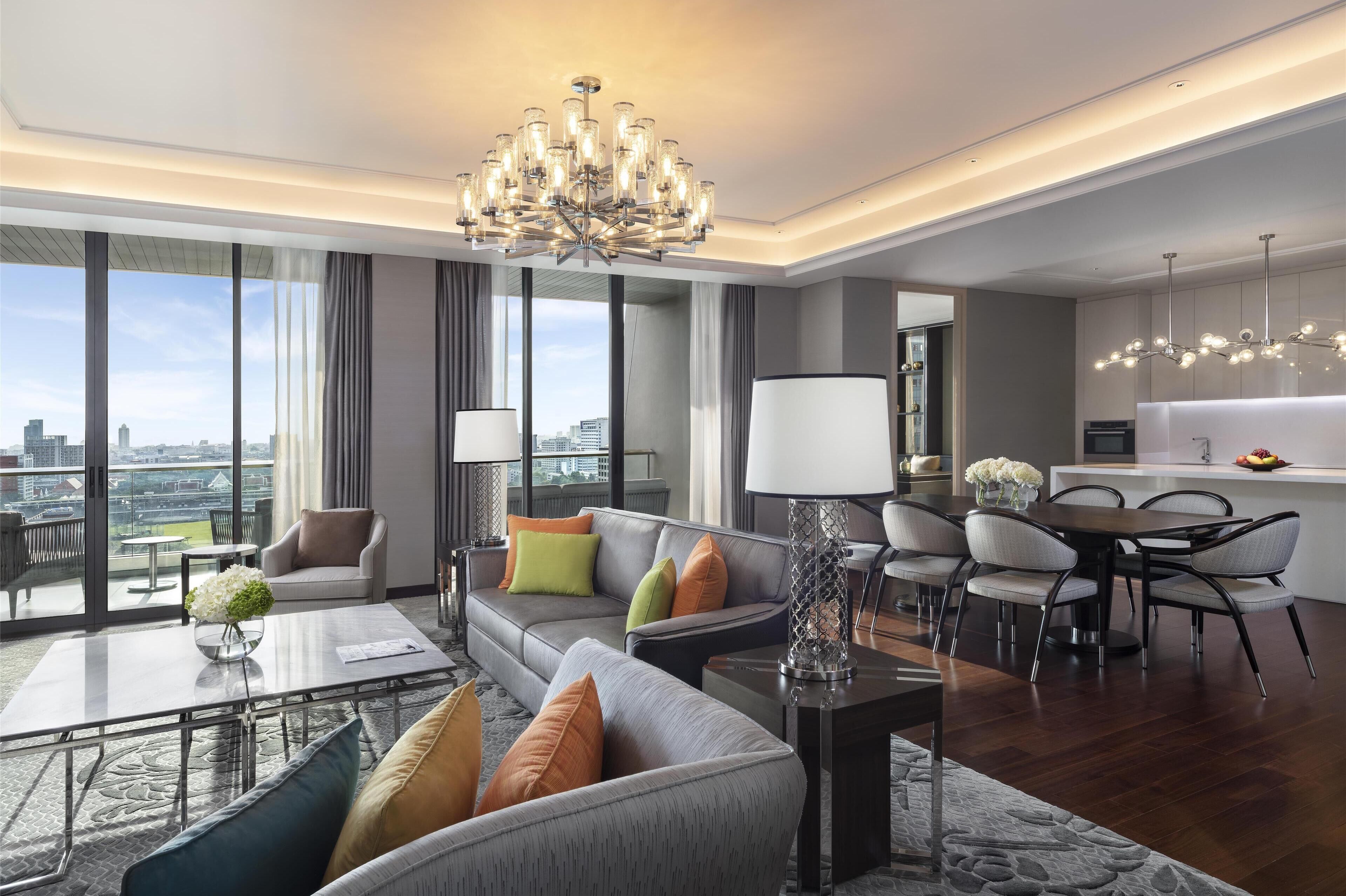Una sala moderna con sofá, mesa de centro y comedor. Hay un ventanal con vista a la ciudad.