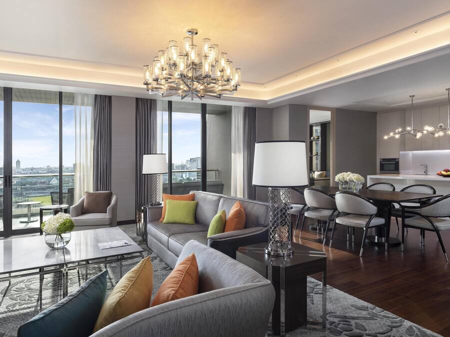 Una sala moderna con sofá, mesa de centro y comedor. Hay un ventanal con vista a la ciudad.