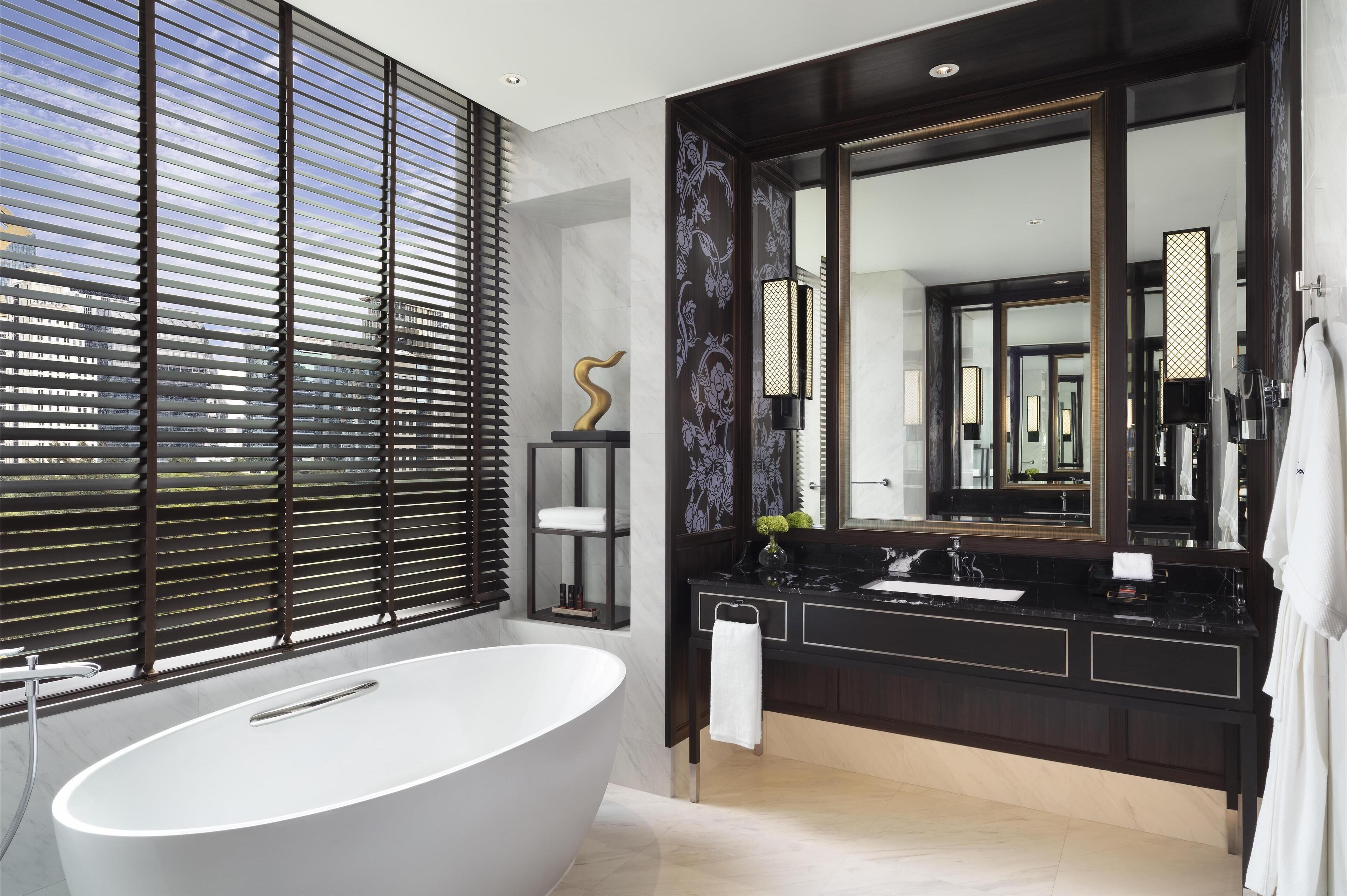 A modern bathroom with a freestanding bathtub, dark wood vanity, and large mirrors.