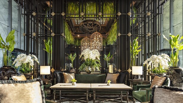 Un lobby lujoso con una zona de estar central, rodeado de techos altos y plantas decorativas.