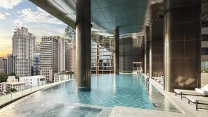 Una piscina infinita en la azotea con vistas a la ciudad, grandes columnas metálicas y sillones de descanso.