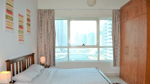 A bedroom with a large bed, a wooden wardrobe, a window with curtains, and artwork on the wall.