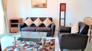 A living room with a brown leather sofa, a glass coffee table, and a patterned rug.