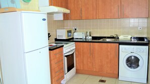 A compact kitchen with wooden cabinets, a white refrigerator, a microwave, a toaster, an oven, and a washing machine.