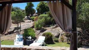 A covered outdoor seating area with two lounge chairs and a table, overlooking a rocky landscape with trees. - COSTA SMERALDA APARTMENT in semi-detached villa with sea view in Cannigione alta (ARZACHENA)