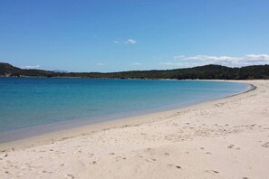 A sandy beach with clear blue water and a forested hill in the background. - COSTA SMERALDA APARTMENT in semi-detached villa with sea view in Cannigione alta (ARZACHENA)