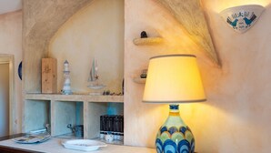 A kitchen with a stone arch, a wooden shelf with decorative items, a lamp, and a wall-mounted light fixture. - COSTA SMERALDA APARTMENT in semi-detached villa with sea view in Cannigione alta (ARZACHENA)