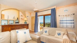 A cozy living room with a sofa and armchairs, a wooden cabinet, and a view of the outdoors. - COSTA SMERALDA APARTMENT in semi-detached villa with sea view in Cannigione alta (ARZACHENA)