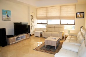 A living room with a flat-screen TV, a beige sofa, a white armchair, and a coffee table. - Stylish 1BR near MOE - MRD (Dubai)