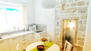 A compact kitchen with a dining area, a stone wall, and a window with a view. - Heart of the City Apartments (Dubrovnik)