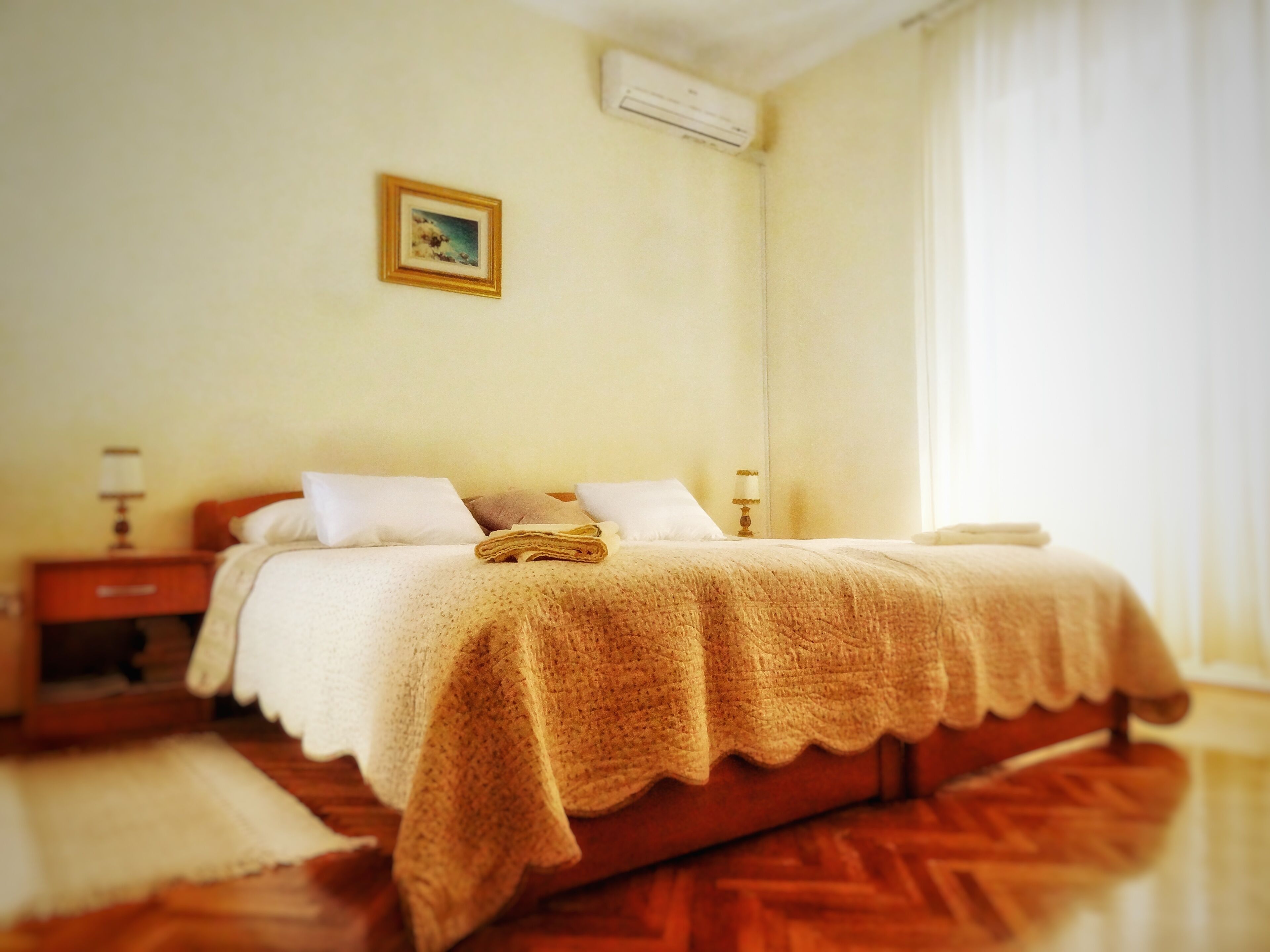 A neatly made bed with a blanket, a bedside table with a lamp, and a small picture on the wall.