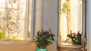 A room with a window, a potted plant, a decorative bowl, and a mirror reflecting the outside view. - Heart of the City Apartments (Dubrovnik)
