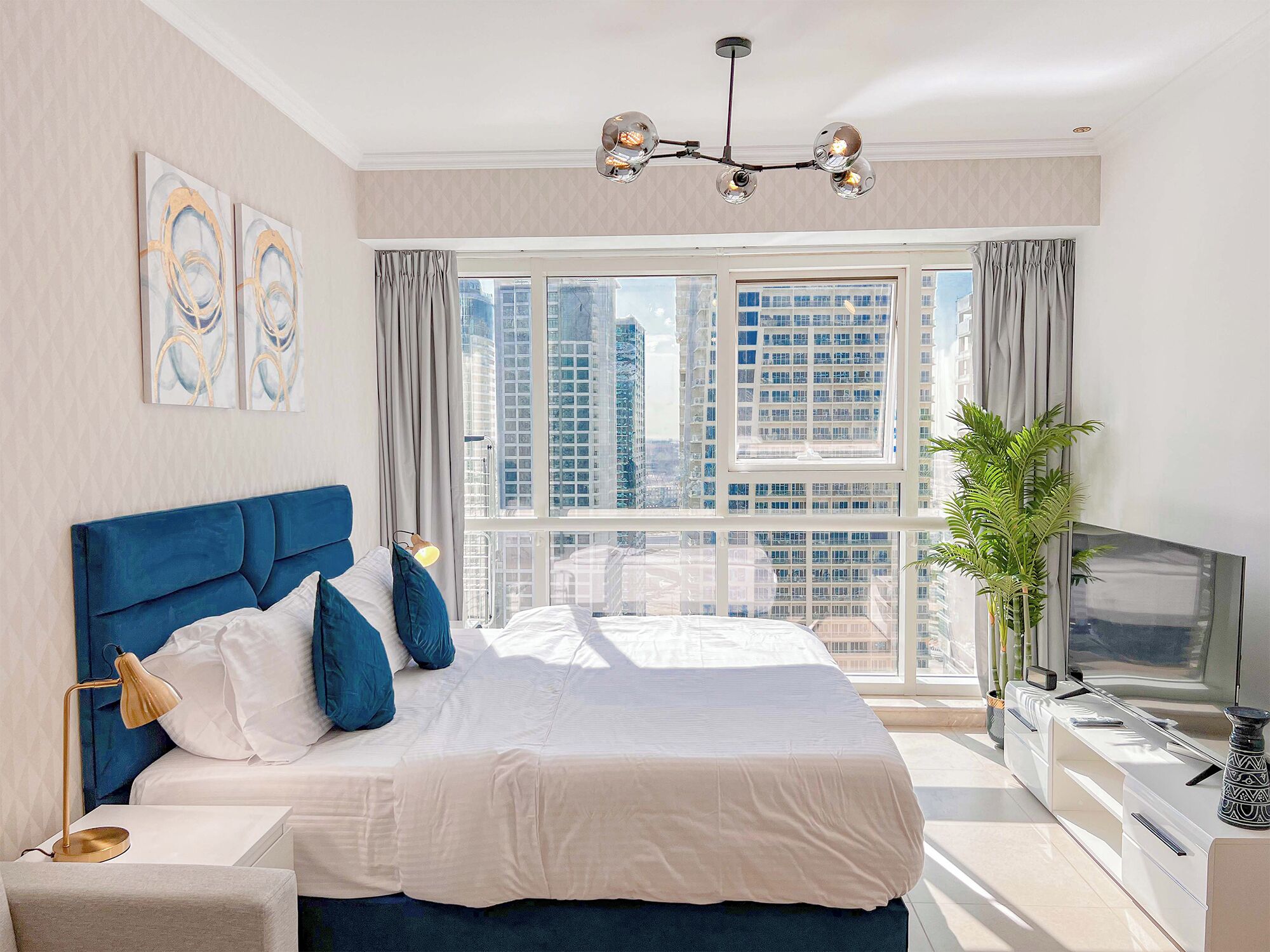 Ein modernes Schlafzimmer mit einem großen Bett, einem Fernseher und Blick auf hohe Gebäude.