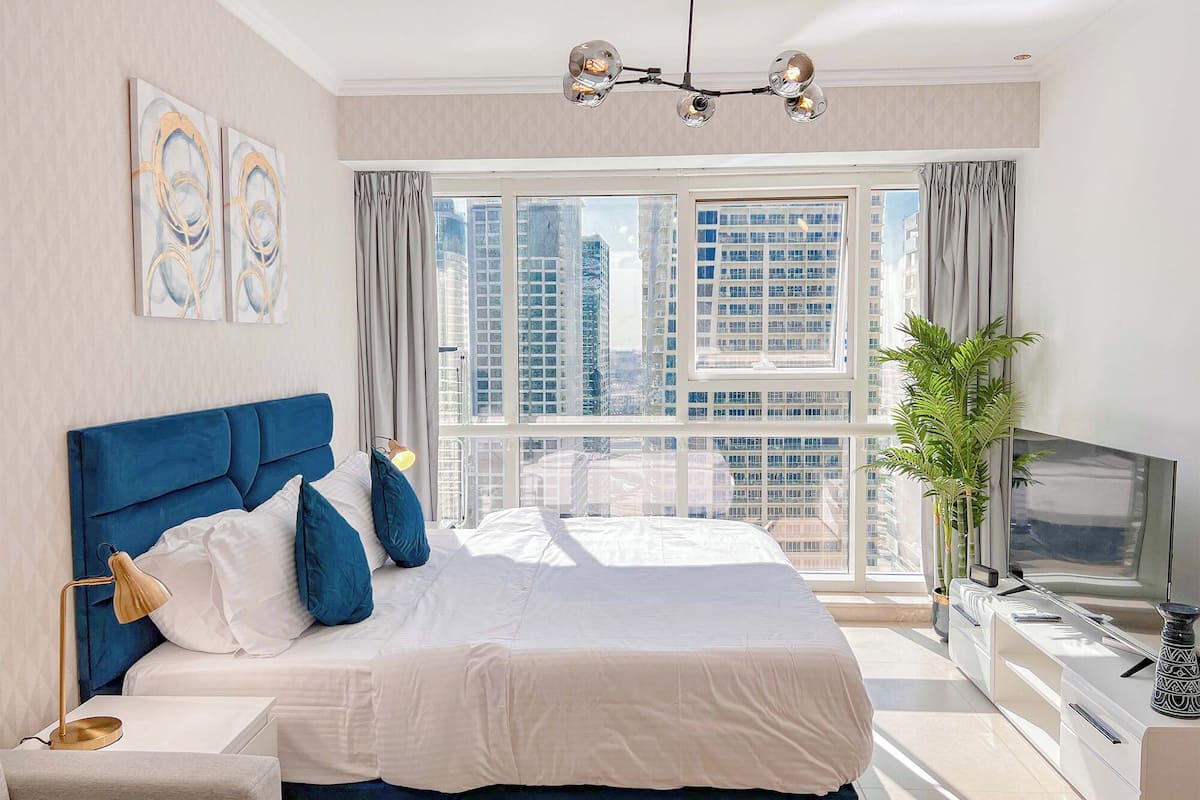 Ein modernes Schlafzimmer mit einem großen Bett, einem Fernseher und Blick auf hohe Gebäude.