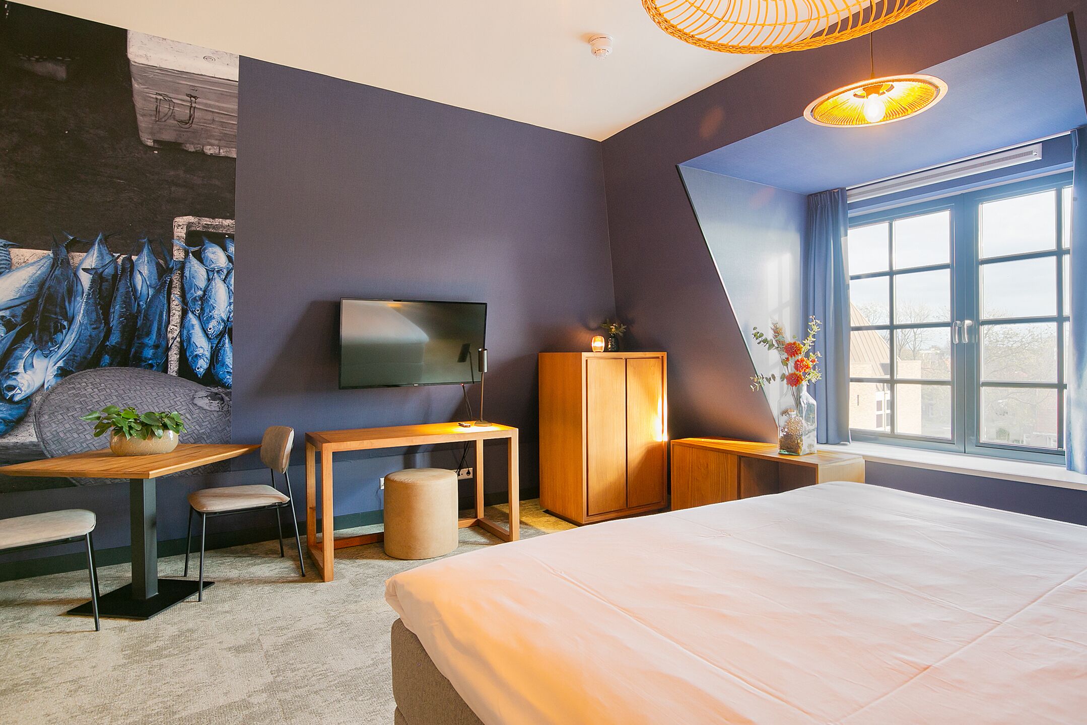 Ein modernes Hotelzimmer mit Bett, Schreibtisch, Sessel, Fernseher und einem großen Fenster mit Ausblick.