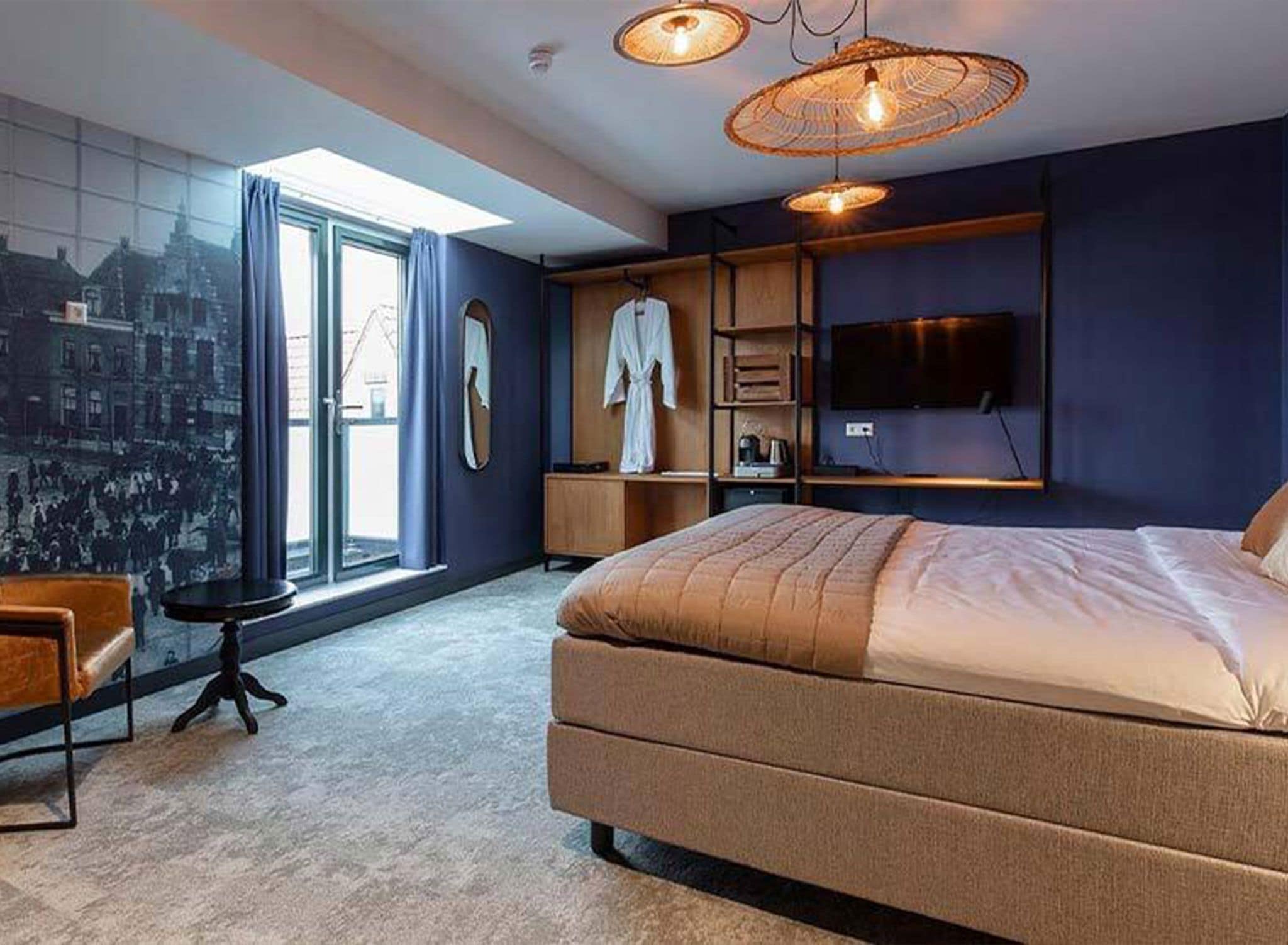 Une chambre moderne avec un grand lit, un téléviseur et une fresque murale représentant un paysage urbain.