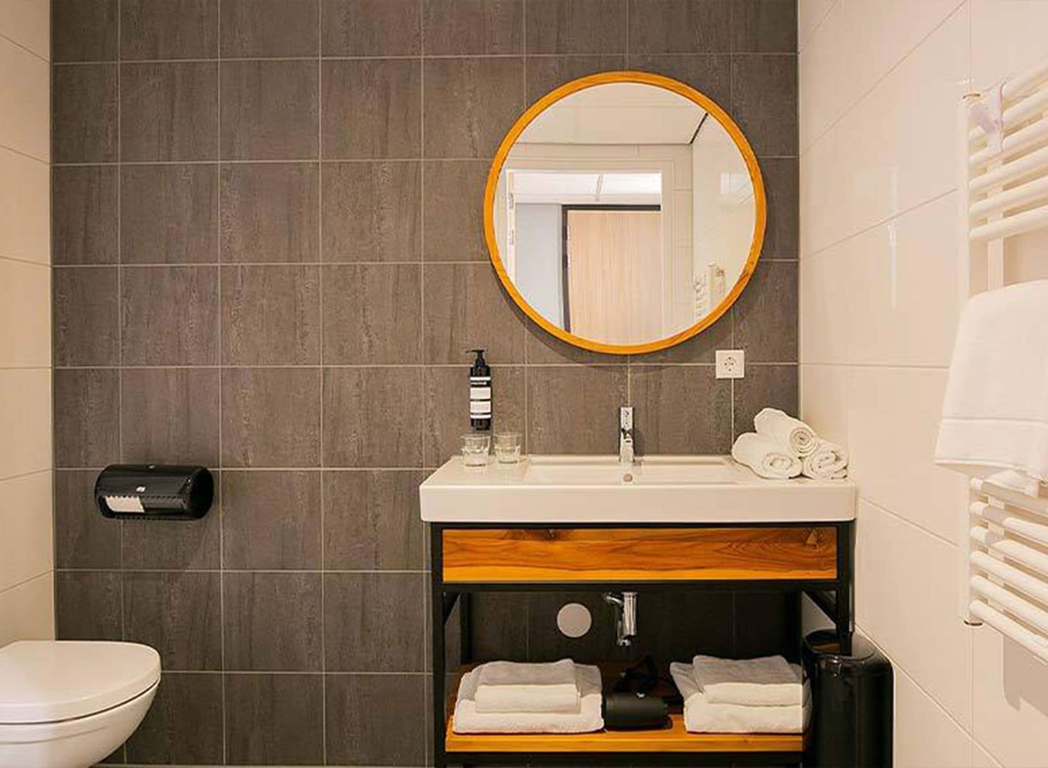 A bathroom with a toilet, sink, mirror, towel rack, and a hand dryer.