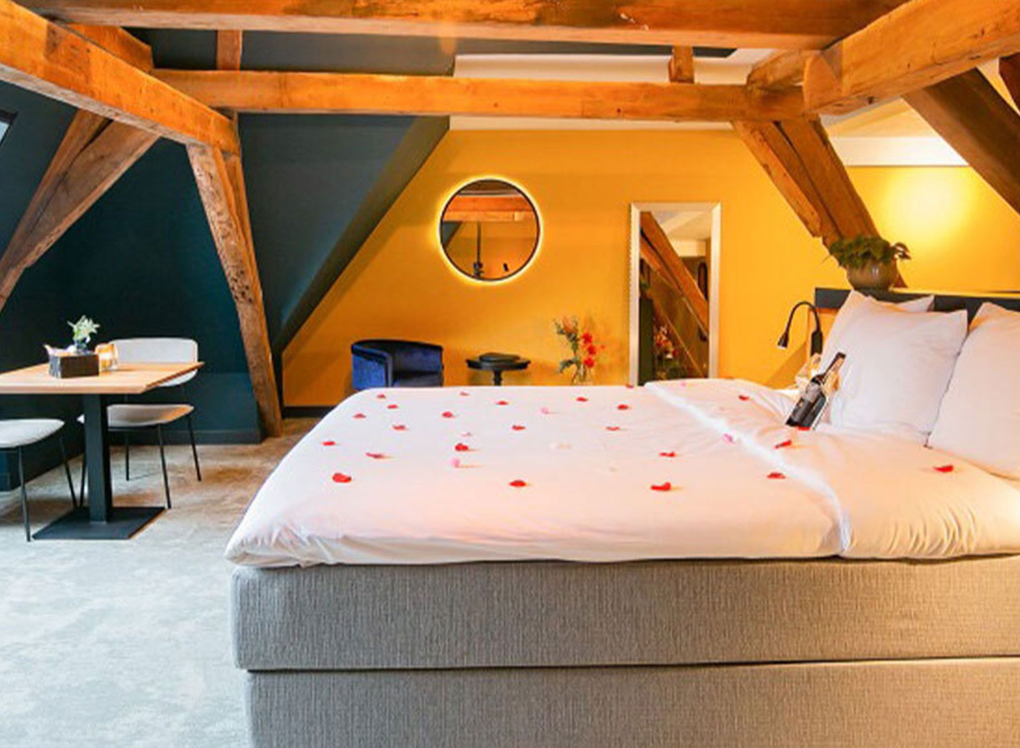 A bedroom with a large bed, a round mirror, a small table, and a chair.