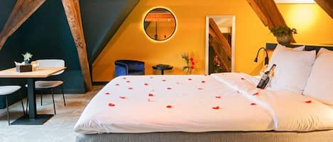 Een slaapkamer met een groot bed, een ronde spiegel, een klein tafeltje en een stoel.