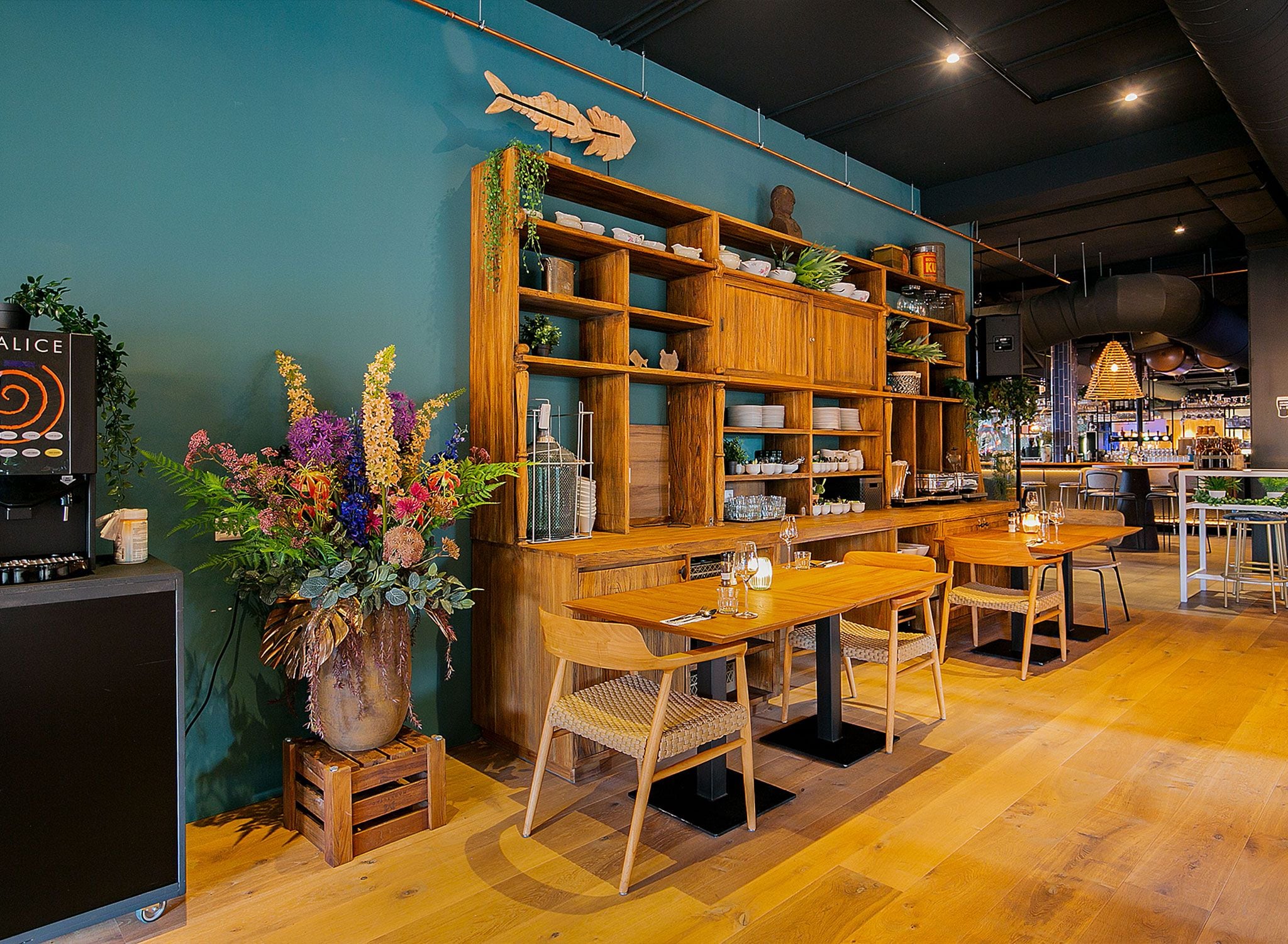 L’intérieur d’un restaurant est aménagé avec des meubles en bois, un coin bar et une variété de plantes.