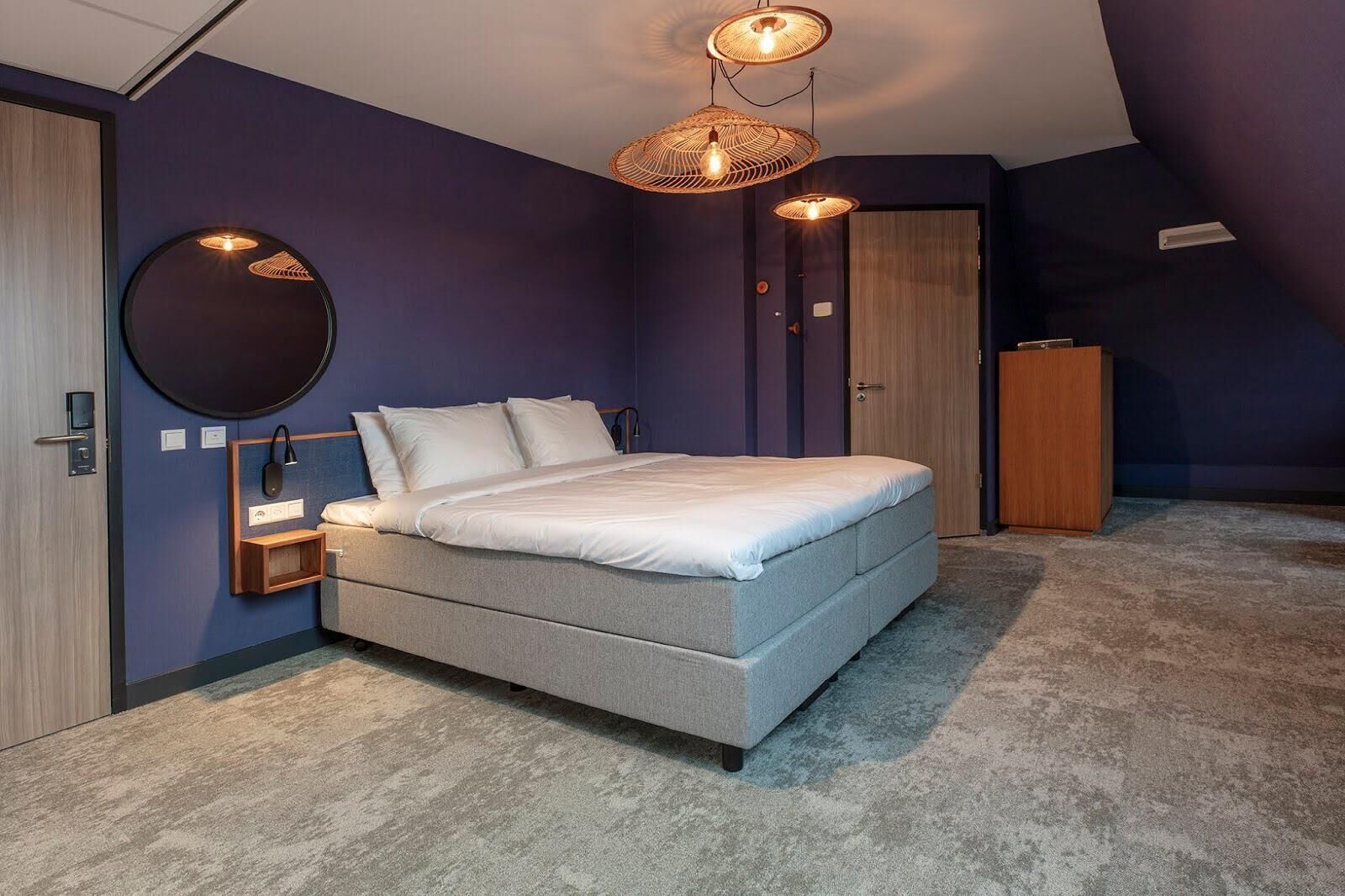 A modern bedroom with a bed, bedside table, wall-mounted mirror, and a wardrobe.