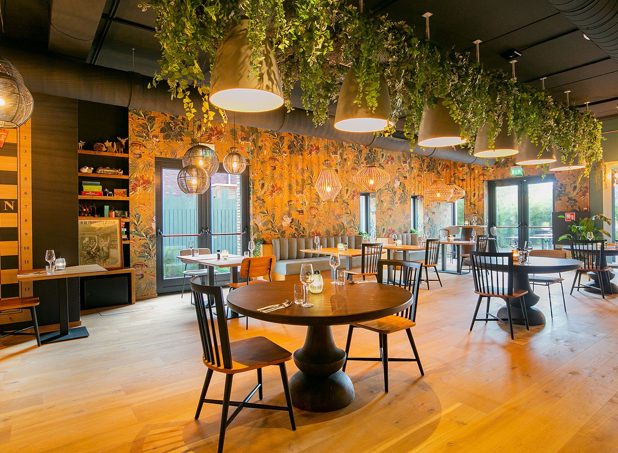 A restaurant with round tables, chairs, hanging plants, and a wooden floor.