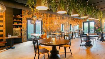 A restaurant with round tables, chairs, hanging plants, and a wooden floor.