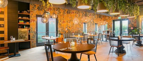 A restaurant with round tables, chairs, hanging plants, and a wooden floor.