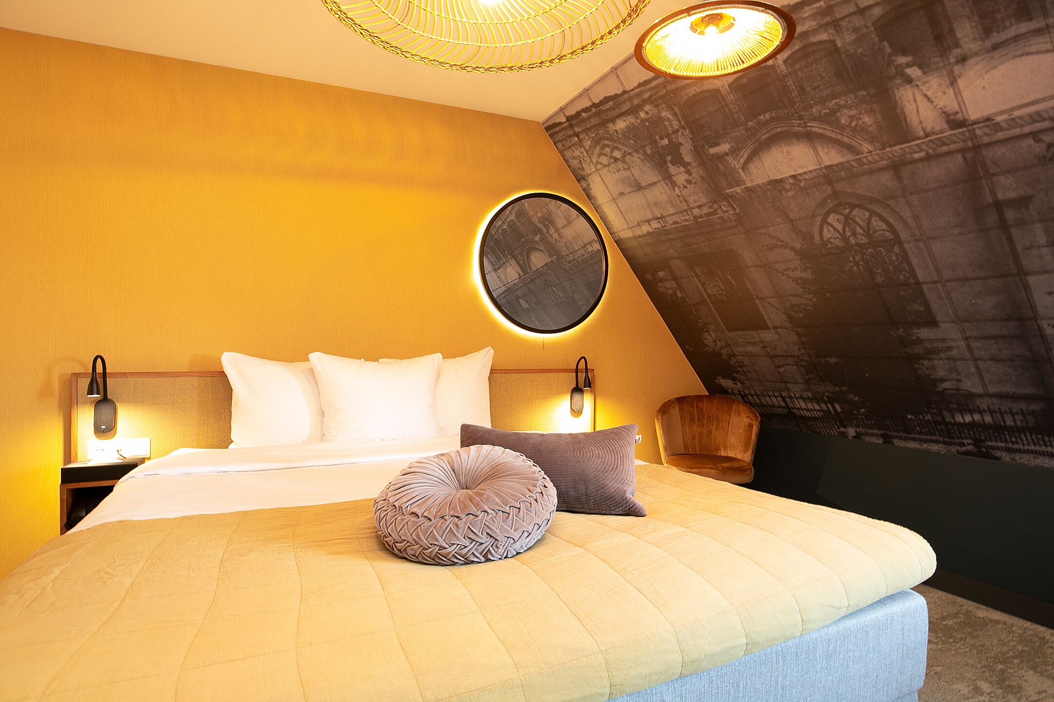 Quarto de hotel com cama, almofadas, tapete redondo e espelho fixado na parede.