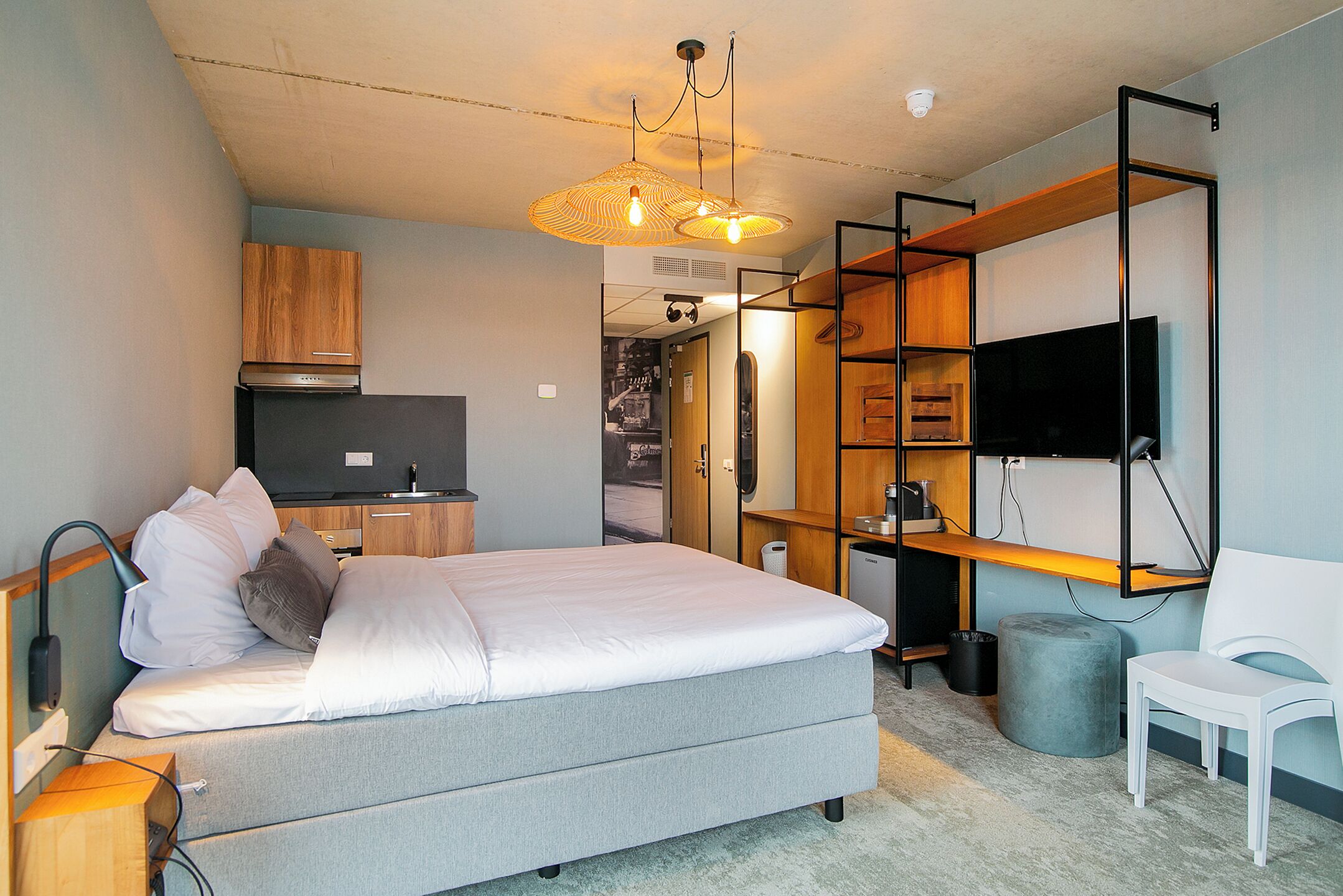 A compact bedroom with a bed, bedside table, TV, and a desk area with shelves.
