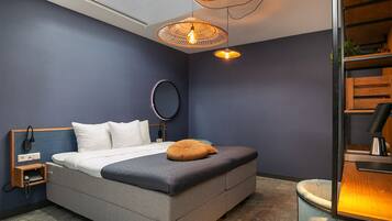 Un dormitorio moderno con cama, mesita de noche, lámpara y un espejo circular en la pared.