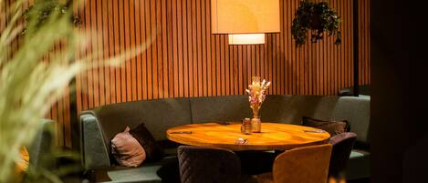 A cozy seating area with a round wooden table, cushioned chairs, and a hanging lamp.