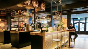 A bar area with shelves of liquor bottles, glasses, and a person reading a menu. - Fletcher Hotel-Restaurant Marktstad-Schagen (Schagen)