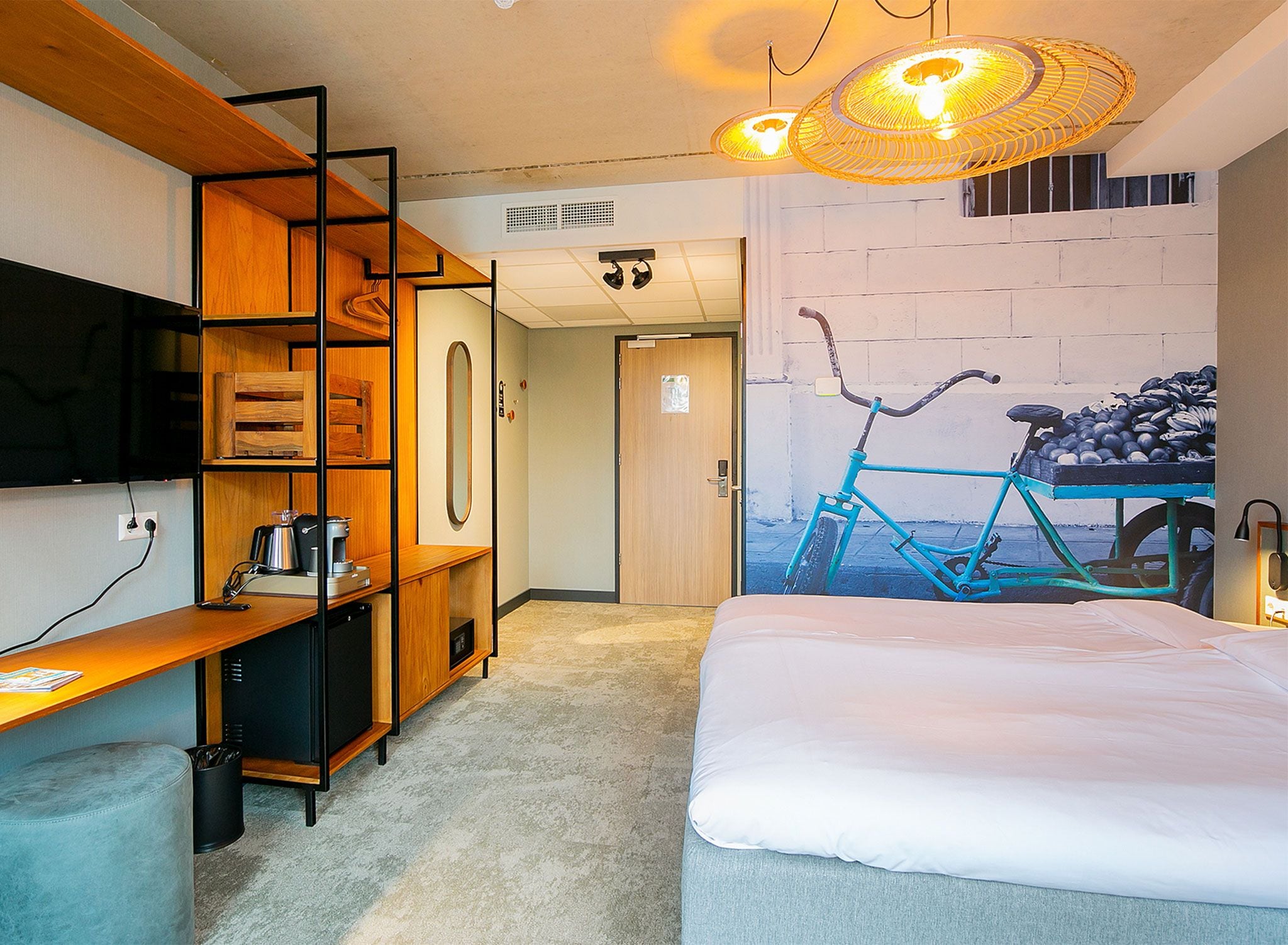 Quarto de hotel moderno com cama, escrivaninha com cafeteira, televisão e um mural de parede exclusivo.