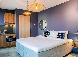 Un dormitorio con cama, mesita de noche, espejo, armario y una pequeña cocina.