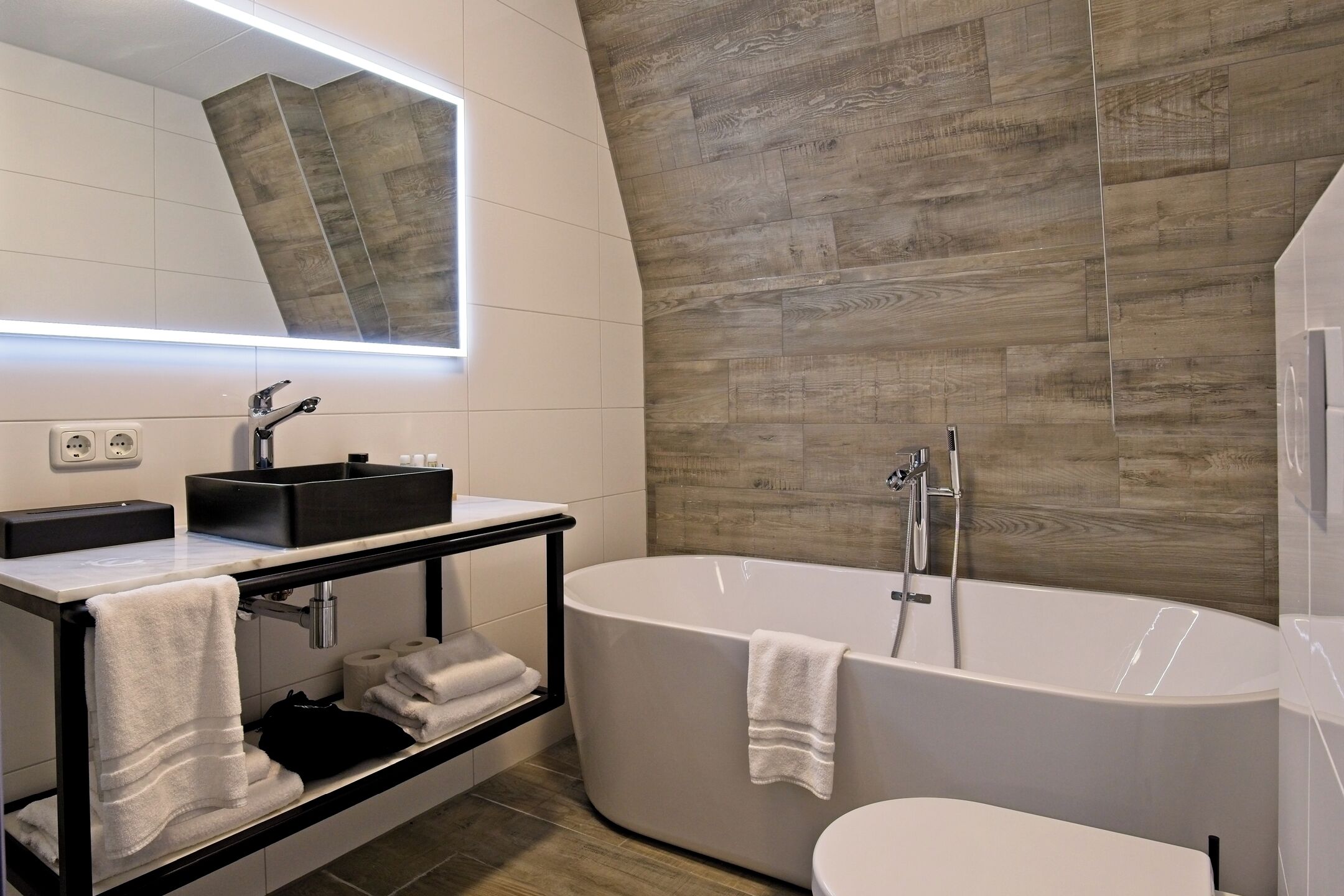 Un baño moderno con una bañera independiente, un tocador con lavamanos negro y un espejo grande.